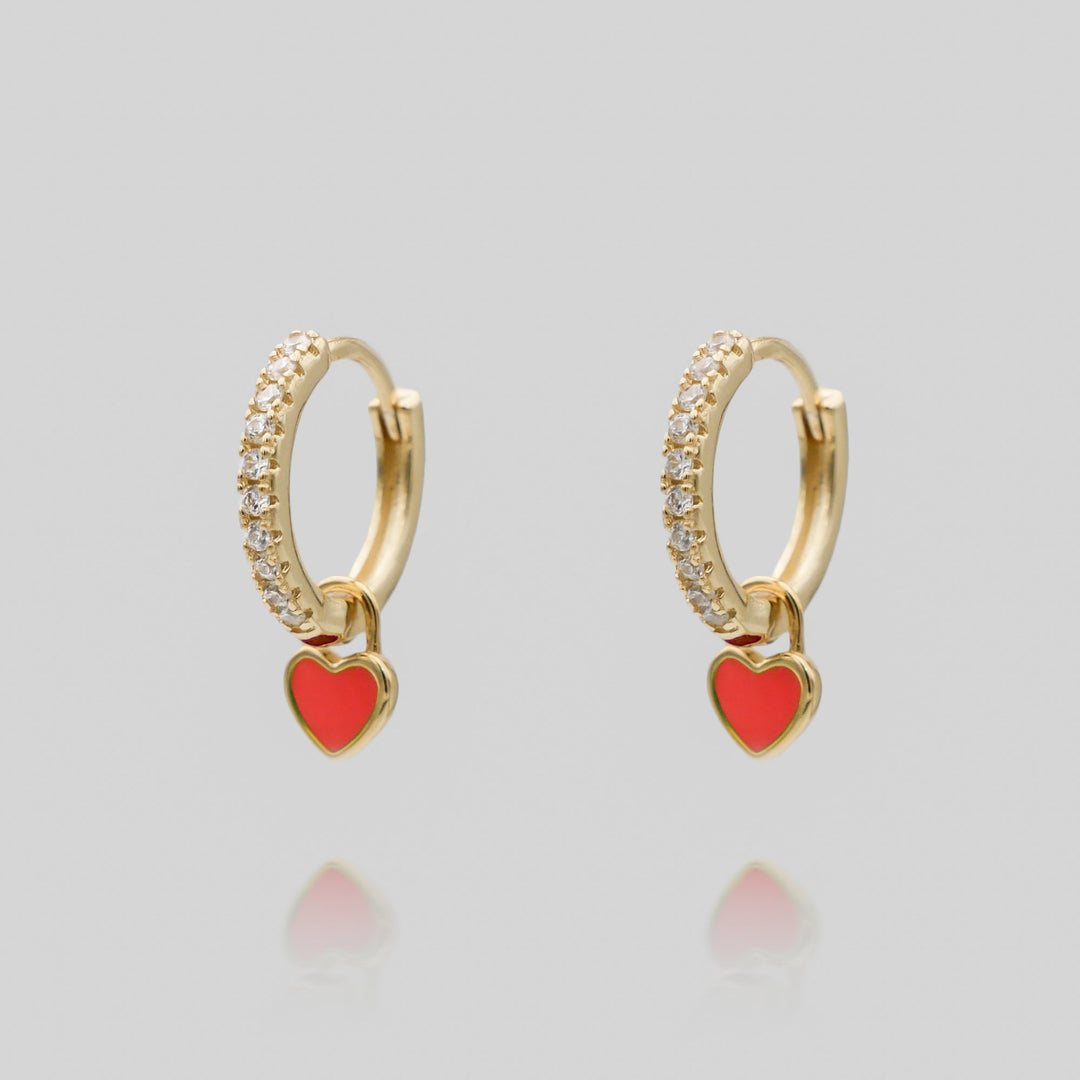 Close-up of a gold plated dainty heart huggie hoop earring, delicate women's jewelry.