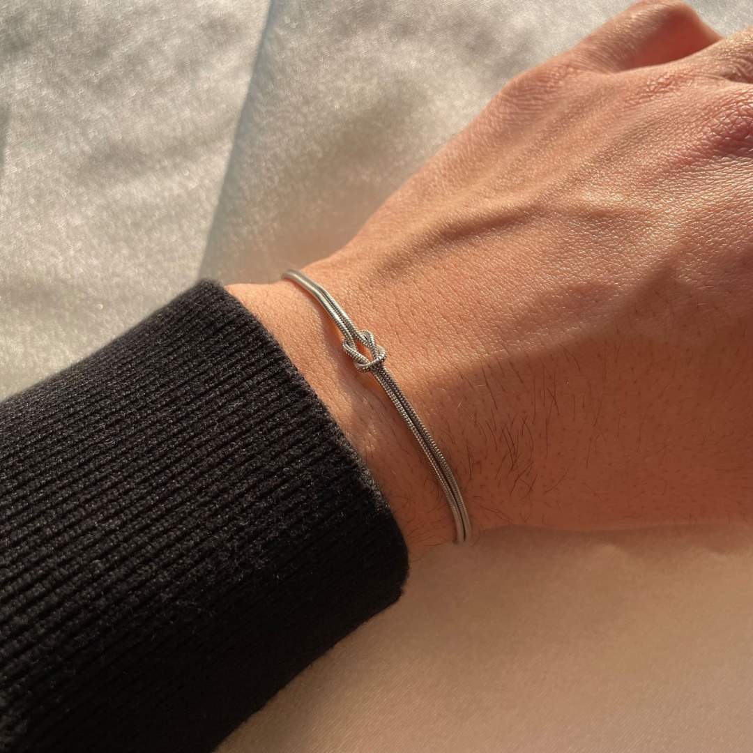 Women's elegant knot bracelet on wrist, subtle gold-tone stainless steel fashion accessory.