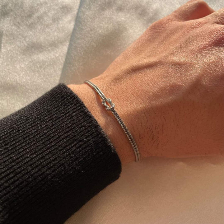 Women's elegant knot bracelet on wrist, subtle gold-tone stainless steel fashion accessory.