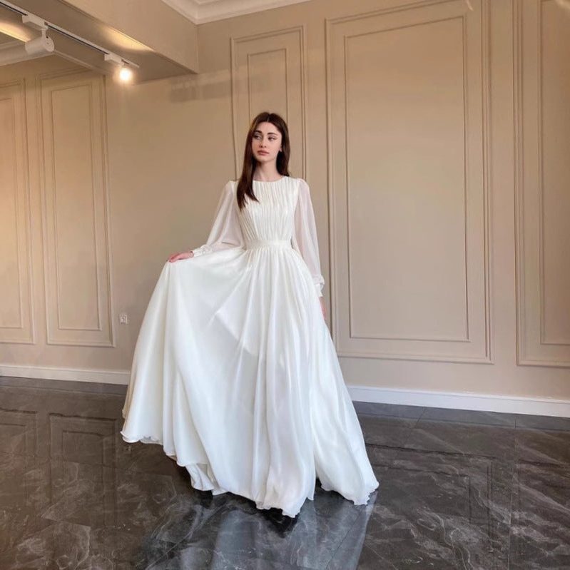 Beautiful white long sleeve maxi dress for women, designed as elegant wedding guest attire. A formal pleated evening gown.