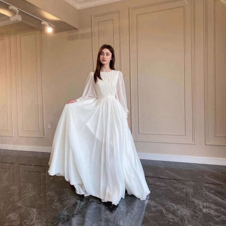 Beautiful white long sleeve maxi dress for women, designed as elegant wedding guest attire. A formal pleated evening gown.