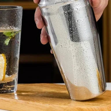 Shiny stainless steel cocktail shaker, jigger, and muddler in a premium home bar kit.