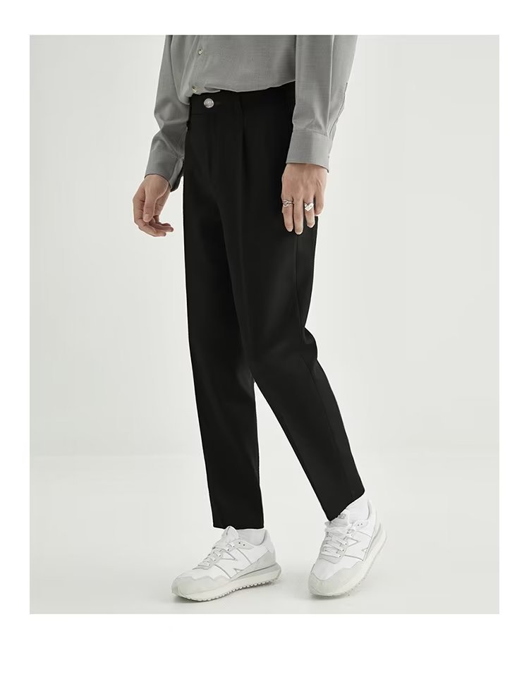 Close-up of men's elegant high-waisted pleated cropped trousers, showcasing fabric and pleat detail.
