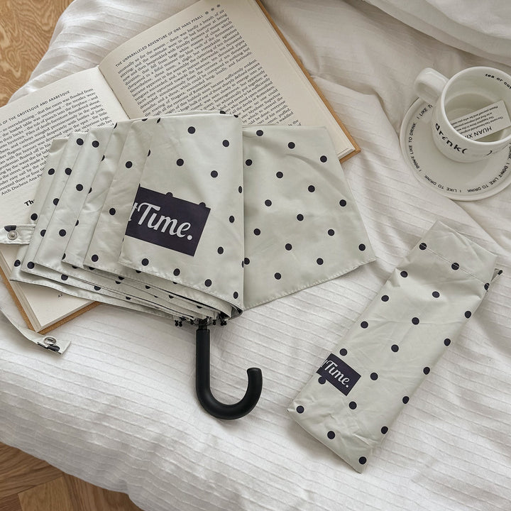 Stylish women's compact umbrella, black with dots, essential for rain.