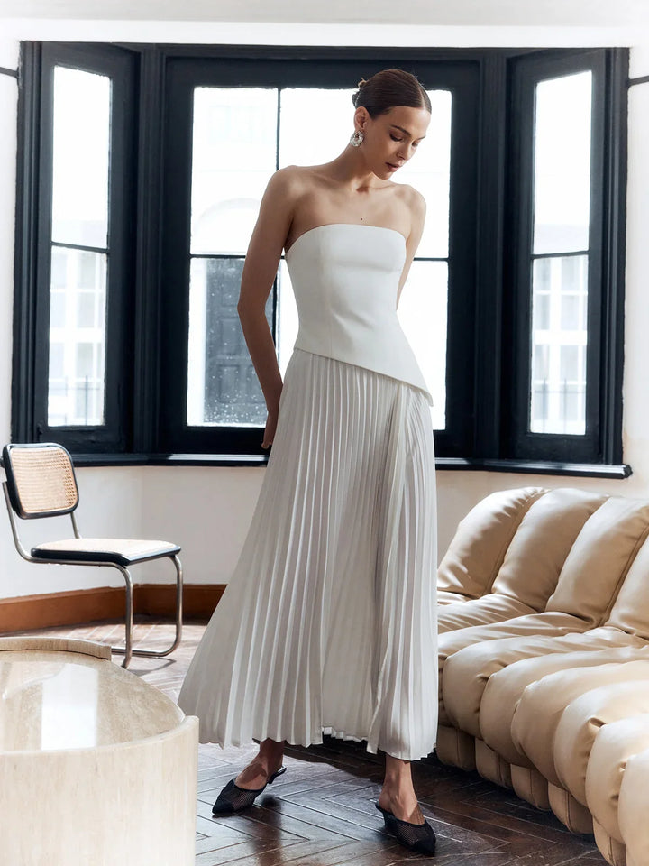 Close-up of the elegant pleated bodice and flowing fabric of the white strapless asymmetric hem maxi dress.