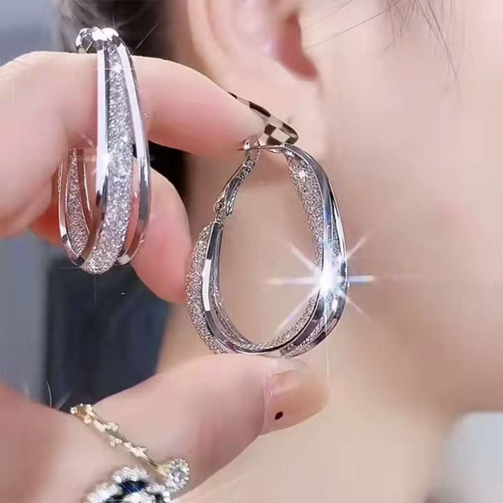 Women's elegant twisted oval hoop earrings with sparkling crystals, a chic fashion accessory.