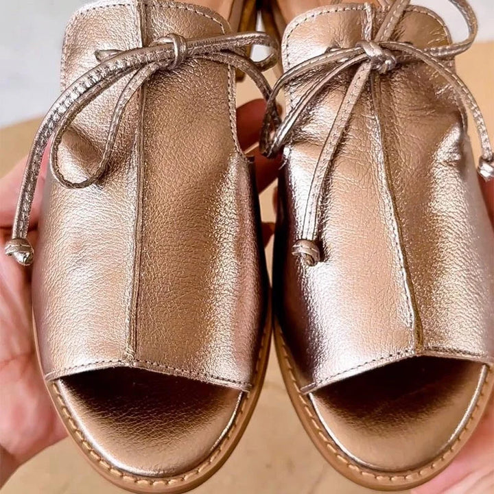 Elegant women's metallic flat sandals with open toe, stylish bow tie & ankle strap, perfect casual summer footwear.