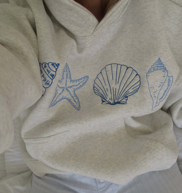 Women's grey seashell print coastal comfort hoodie, relaxed fit pullover with drawstring hood for beach fashion.