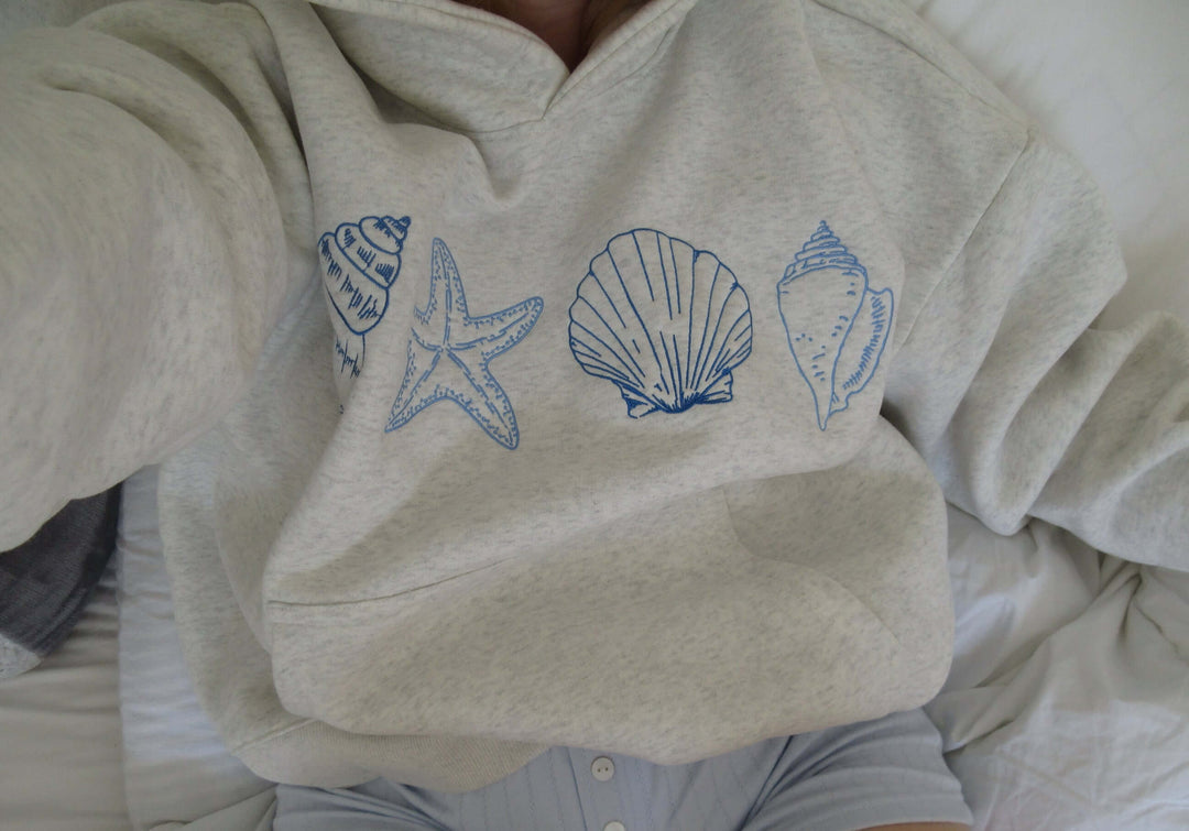 Grey women's hoodie featuring a stylish seashell print, a comfortable casual pullover for coastal living & everyday wear.