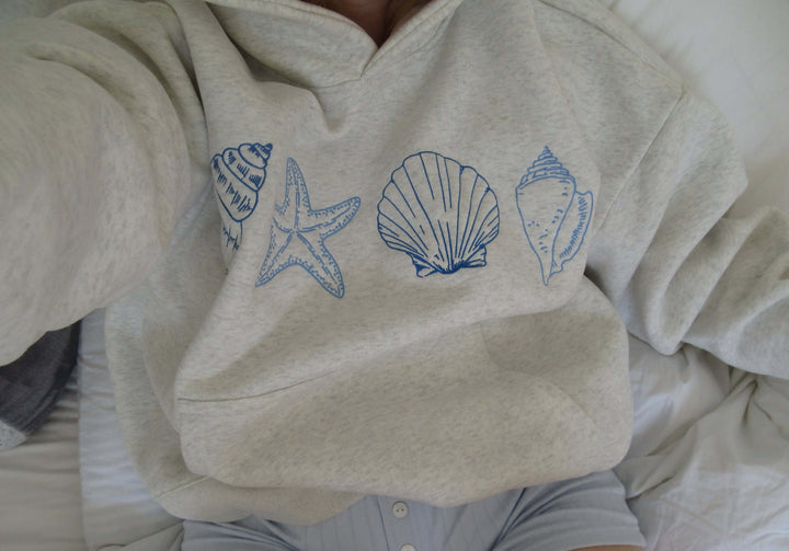 Grey women's hoodie featuring a stylish seashell print, a comfortable casual pullover for coastal living & everyday wear.