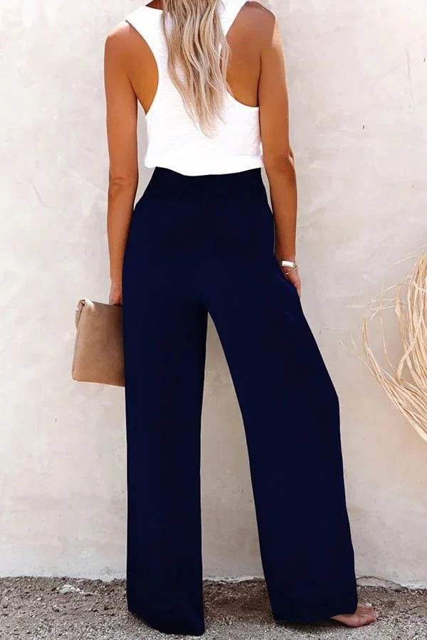 Woman models high-waisted wide-leg trousers with smocked button front, styled for a relaxed summer day.