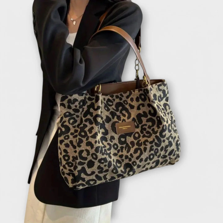 Chic leopard print women's shoulder bag featuring comfortable faux-leather handles. Fashionable animal print accessory.