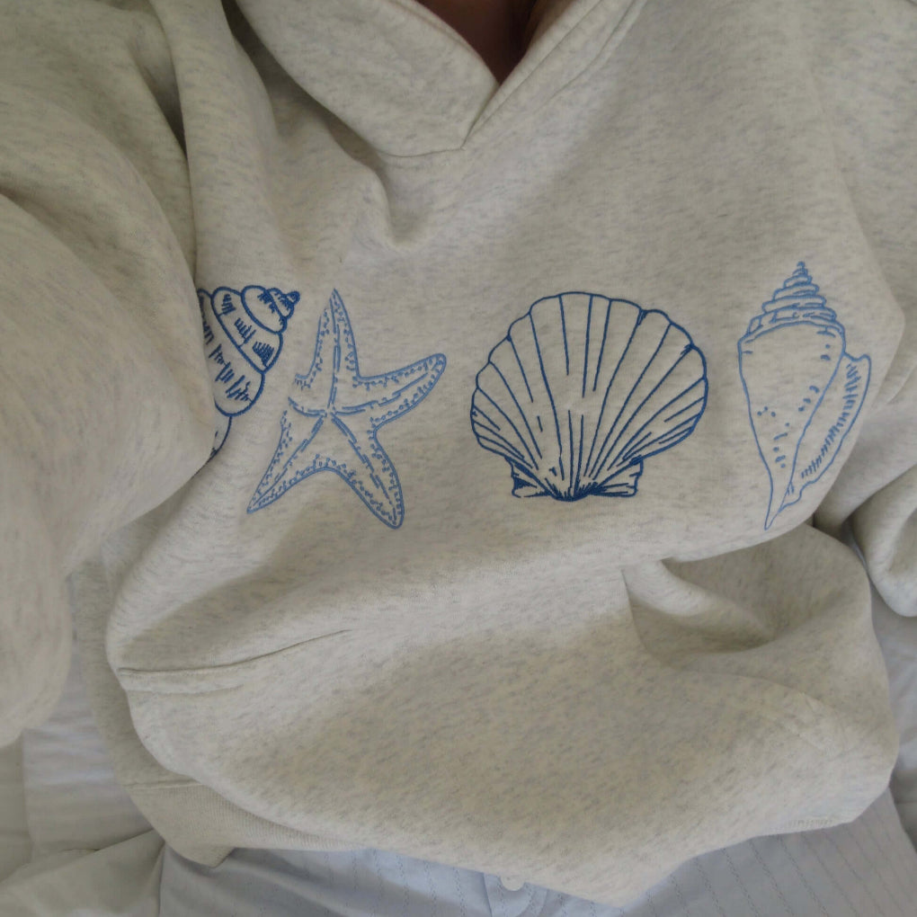 Women's seashell print hoodie with drawstring hood & kangaroo pocket for coastal comfort. Relaxed fit beachwear.