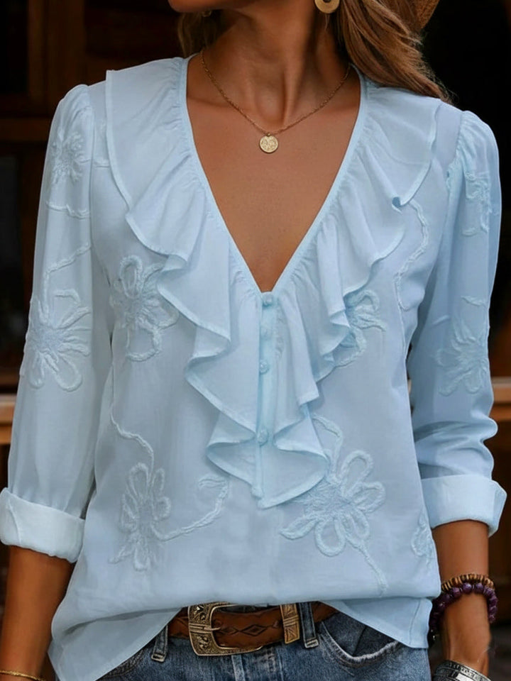 Close-up of a women's vintage V-neck shirt, showcasing detailed floral embroidery and soft frill accents.