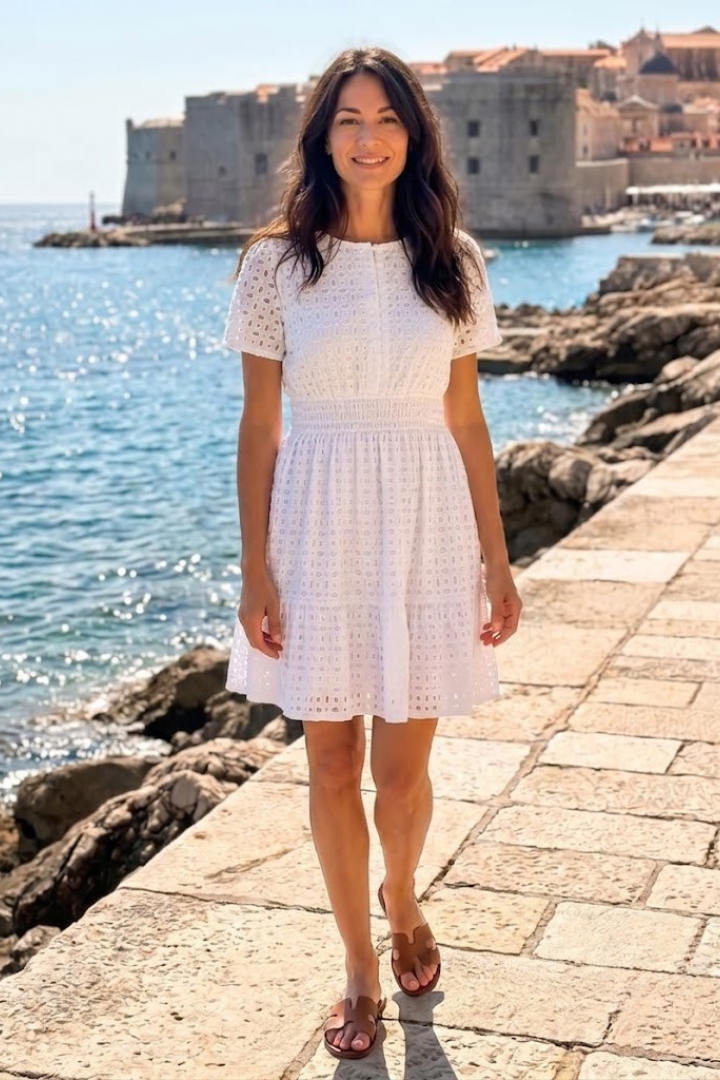 Close-up: White eyelet mini dress showcasing intricate embroidery & soft flutter sleeves for women.